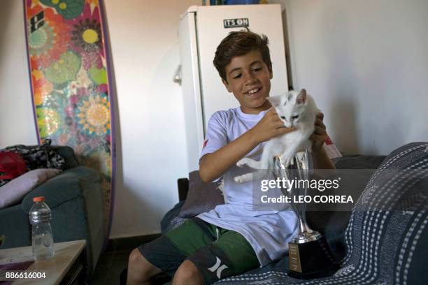 Young surfer Rickson Falcao jokes with his cat and one of his trophies at his house in Saquarema, Rio de Janeiro state, Brazil on November 29, 2017....