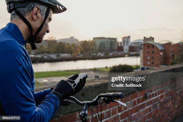 un hombre mirando su teléfono a horcajadas en su ciclo - barrier highway fotografías e imágenes de stock