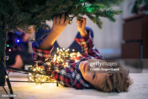 kleiner junge einen weihnachtsbaum lichter aufsetzen - miteinander verbunden stock-fotos und bilder