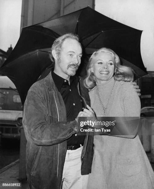 Actors Michael Bryant and Carroll Baker pose under an umbrella in Cricklewood, London, 14th January 1970. They star together in the BBC television...