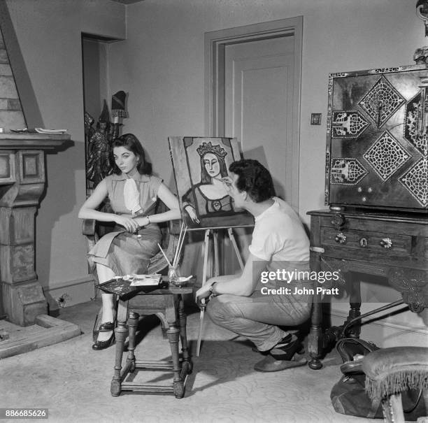 Actor Maxwell Reed paints a portrait of his wife, actress Joan Collins, wearing a crown, at their flat in Hanover Square, London, 8th May 1953.