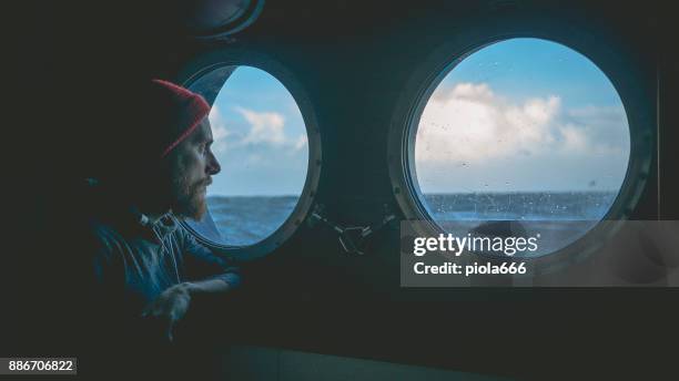 man op de patrijspoort venster van een vaartuig in een ruwe zee - viewpoint stockfoto's en -beelden