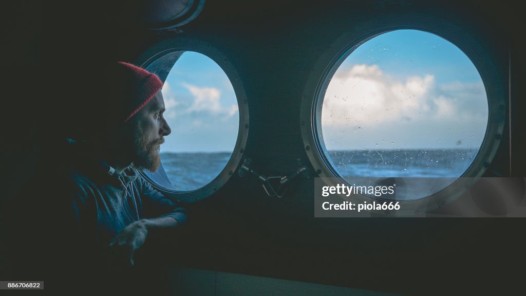 Man at the porthole window of a vessel in a rough sea