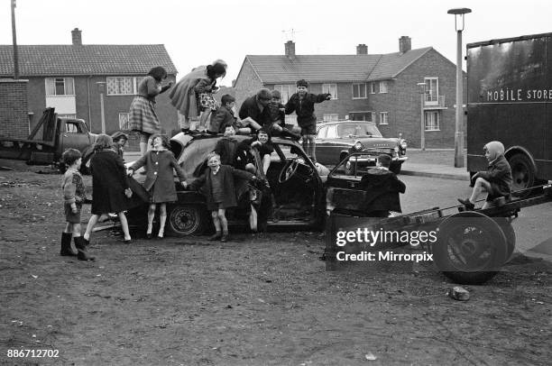 Children play on the wreck of a dumped car at Kirkby, Liverpool, 18th March 1965.