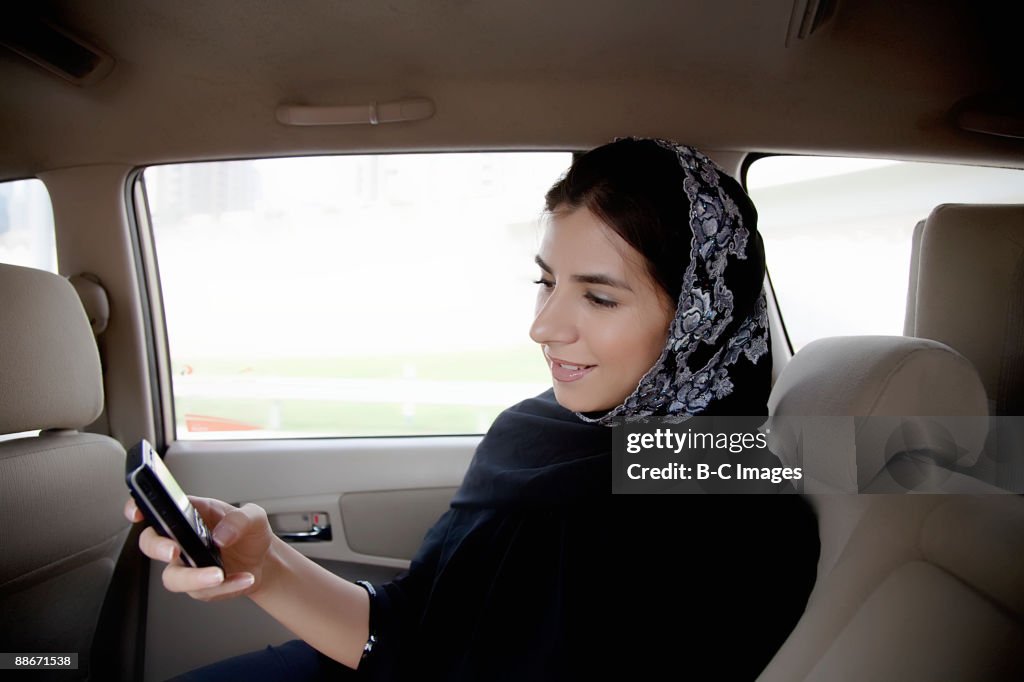 Woman in a taxi text messaging with a mobile phone, Dubai, UAE.