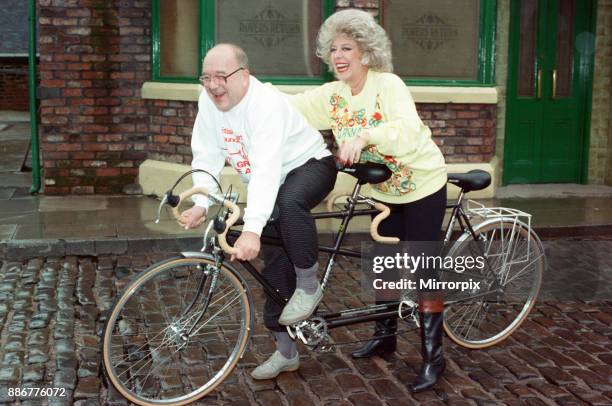 Julie Goodyear and Roy Barraclough pictured on a tandem bike on the set of Coronation Street, 13th February 1990.