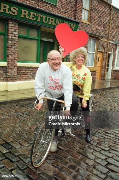 Julie Goodyear and Roy Barraclough pictured on a tandem bike on the set of Coronation Street, 13th February 1990.