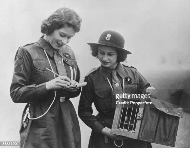 Princess Elizabeth writes a message to Chief Guide Lady Olave Baden-Powell as her younger sister Princess Margaret Rose looks on, 20th February 1943....
