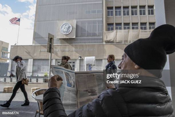 Man reads a newspaper as he sits in a café outside the US embassy in Tel Aviv on December 6, 2017. - President Donald Trump is set to recognise...