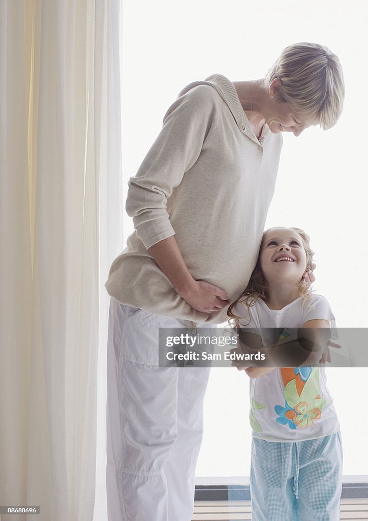 Daughter listening to pregnant mothers stomach