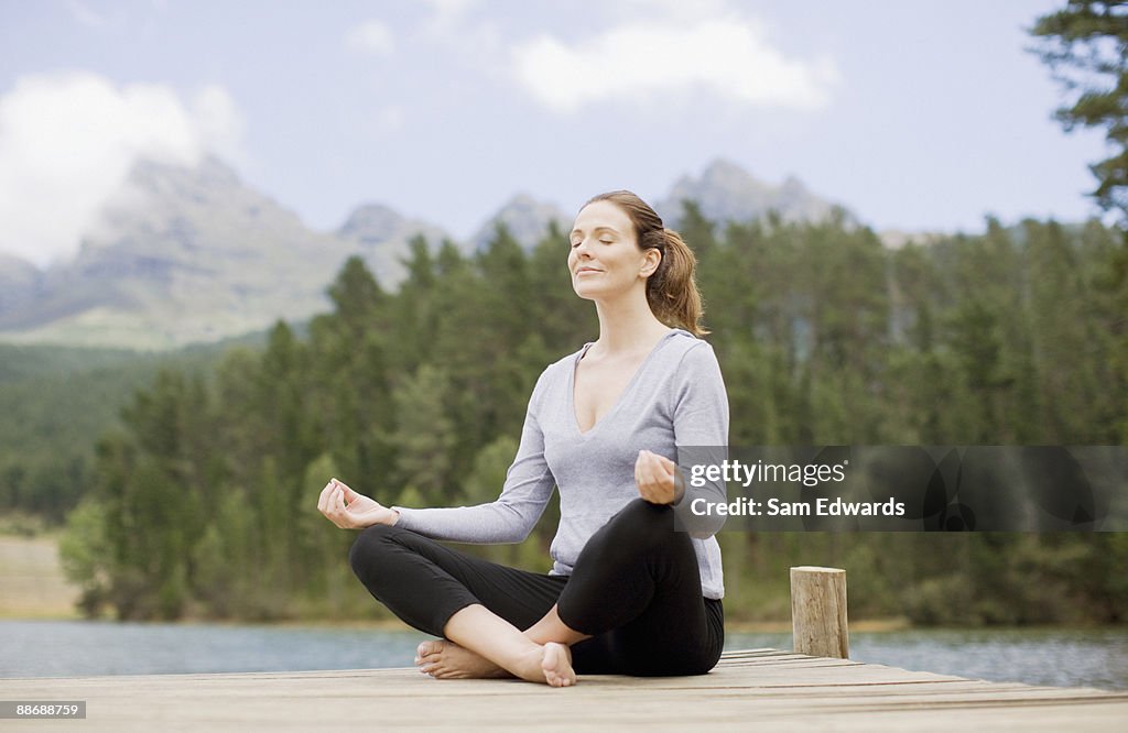 Woman practicing yoga on pier by lake