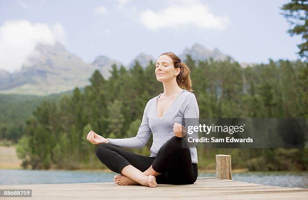 woman practicing yoga on pier by lake - cross legged barefoot stock pictures, royalty-free photos & images
