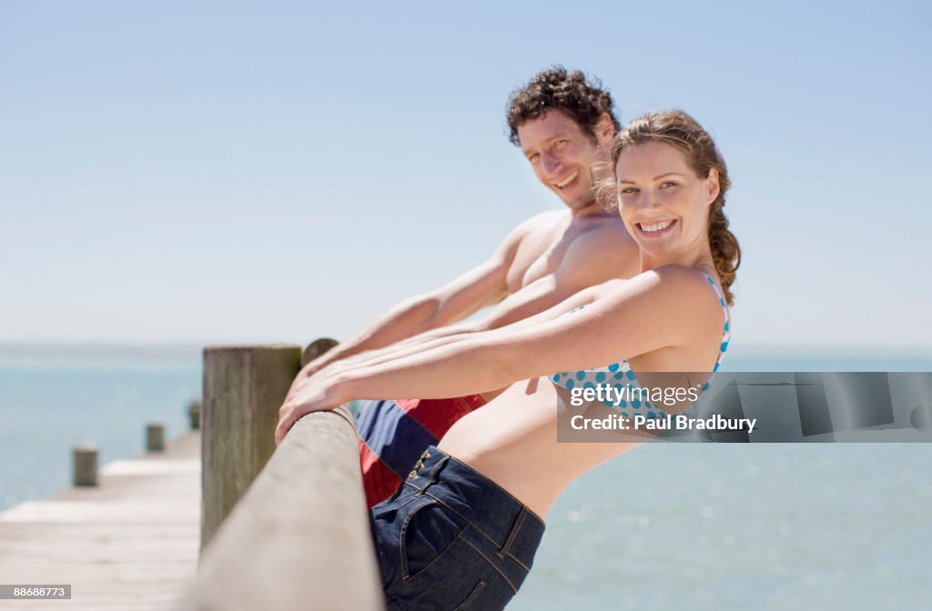 Couple leaning off pier at ocean