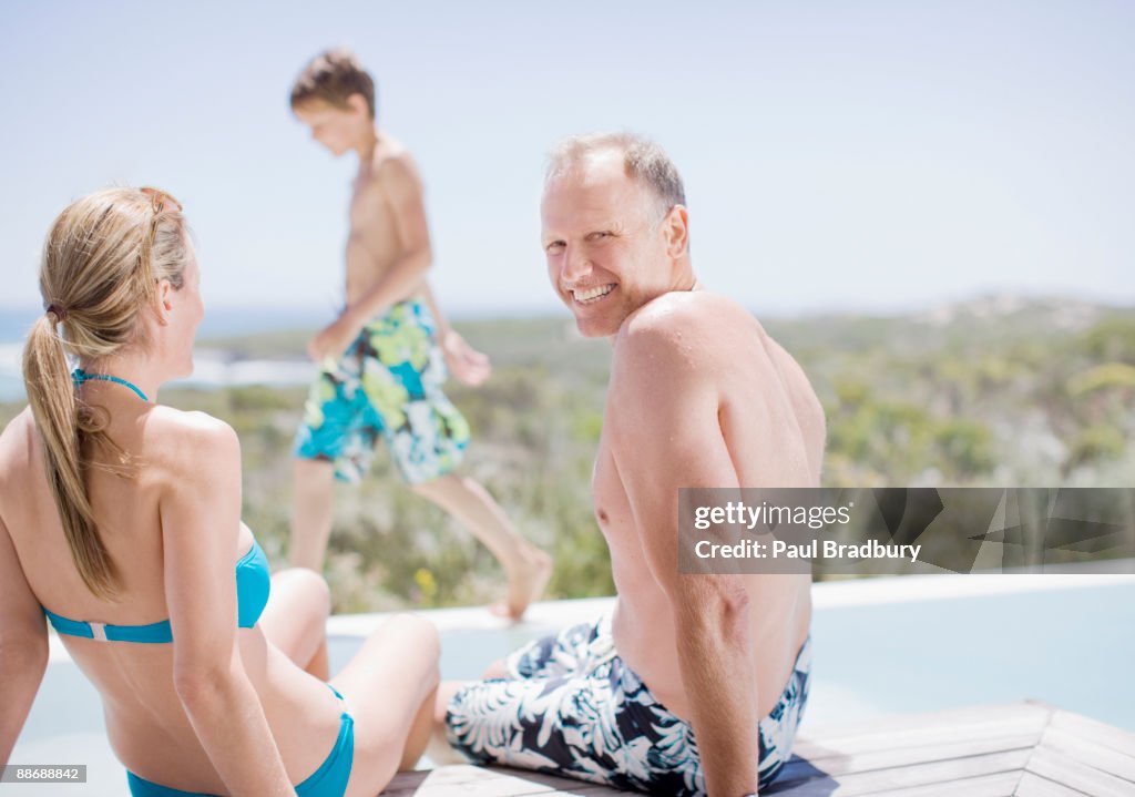 Family sitting by swimming pool