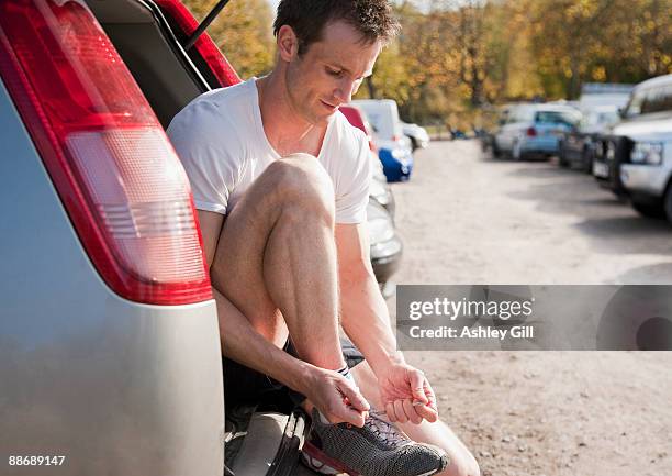 man tying shoes in hatchback of car - ashley cooper - fotografias e filmes do acervo