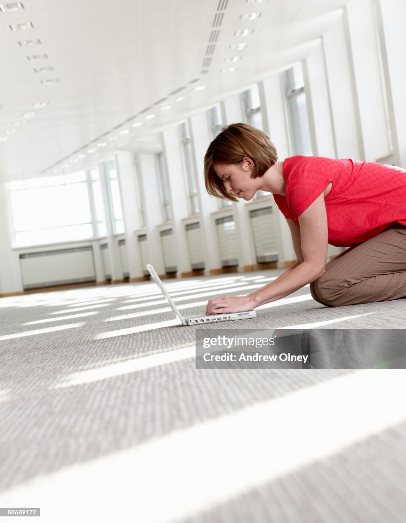 Businesswoman using laptop on floor in empty office