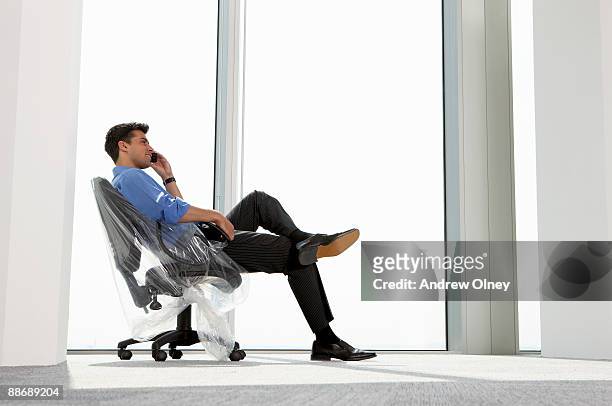 businessman talking on cell phone on wrapped chair - man wrapped in plastic stock pictures, royalty-free photos & images