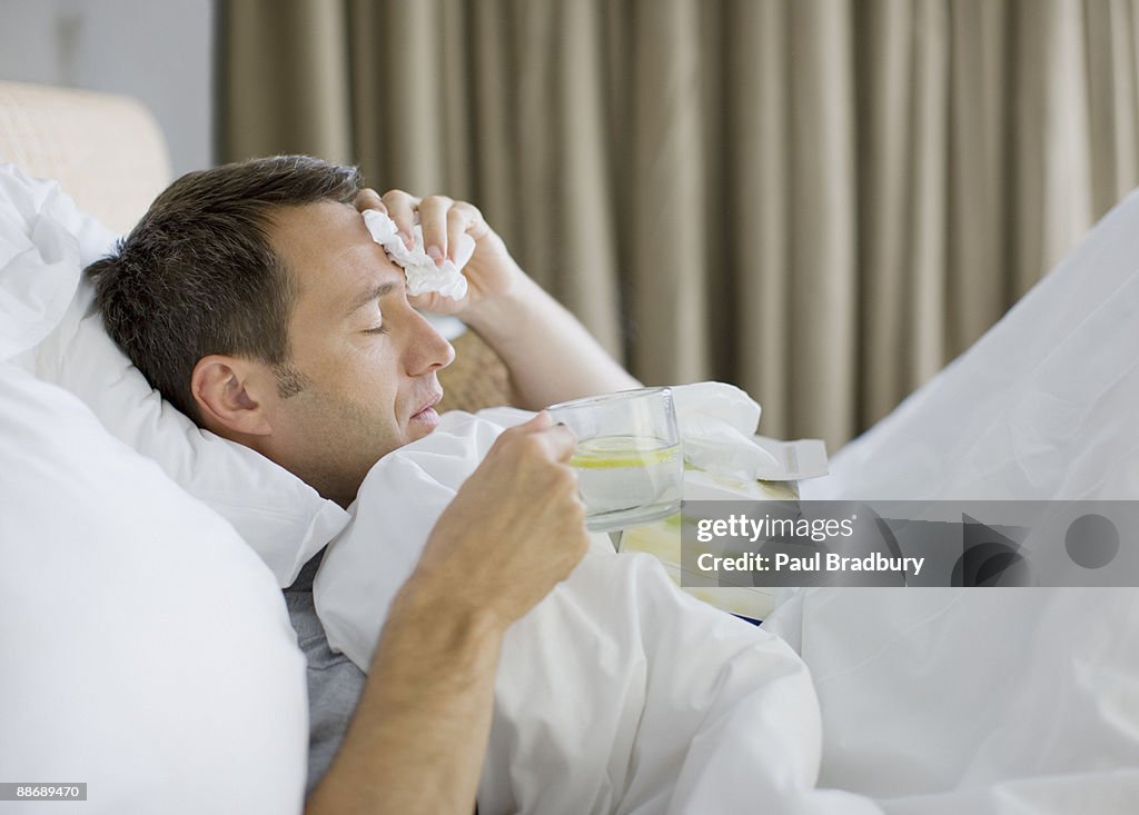 Krank im Bett Mann trinkt heißes Getränk
