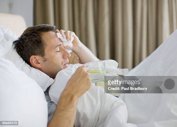krank im bett mann trinkt heißes getränk - krankheit stock-fotos und bilder