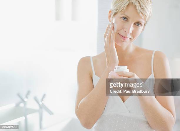 mujer aplicar crema facial en la mañana - crema facial fotografías e imágenes de stock