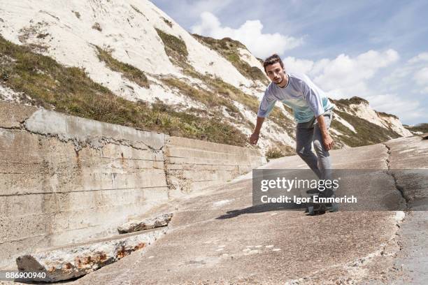 young male skateboarder skateboarding down cliff sea wall - フォークストーン ストックフォトと画像