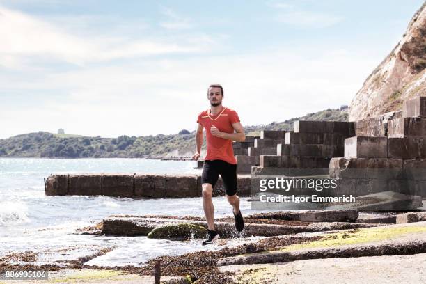 young male runner running along waters edge of sea defence - igor emmerich stock pictures, royalty-free photos & images
