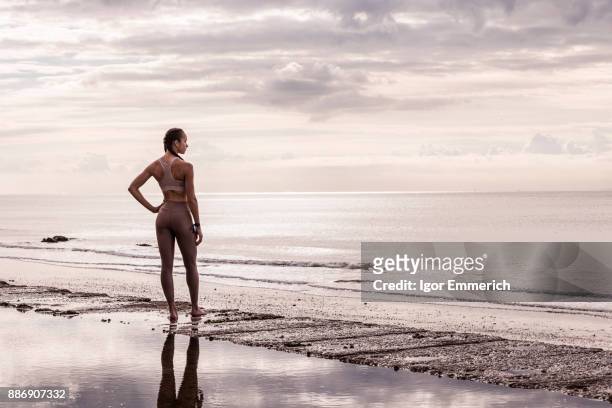 young female runner at waters edge looking out to sea - igor emmerich stock pictures, royalty-free photos & images