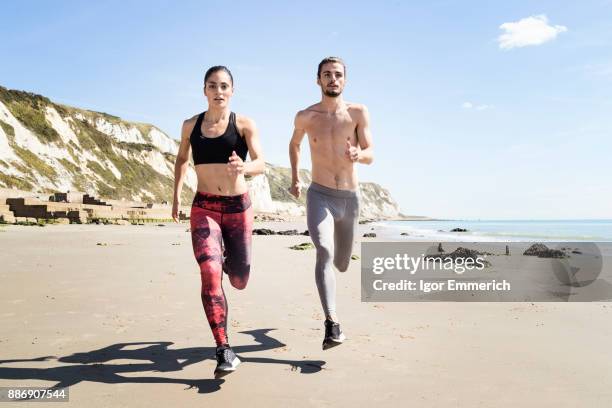 young man and woman running along beach, front view - igor emmerich stock pictures, royalty-free photos & images