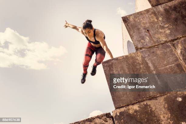 young female free runner jumping down sea wall - stödjemur bildbanksfoton och bilder