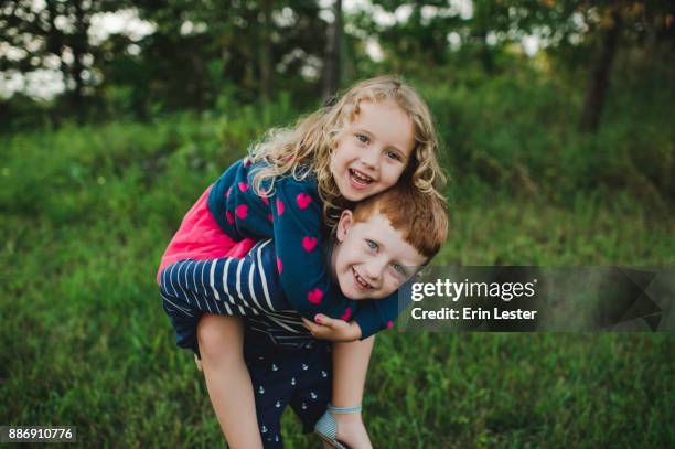 portrait of boy giving sister a piggyback in field - 8 girls no cup stock-fotos und bilder