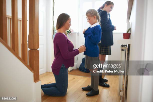 Woman fastening daughters school cardigan in hallway