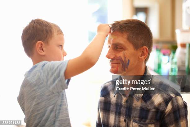 young boy drawing on fathers face using face paint - face paint kids fotografías e imágenes de stock