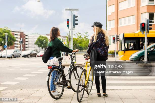 two young women pushing bikes in town - bus lane stockfoto's en -beelden