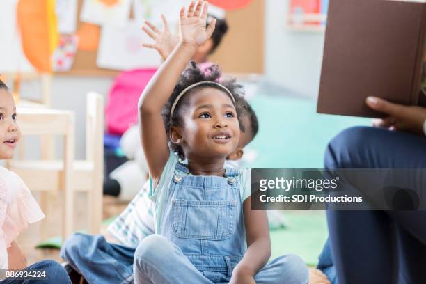 niña levanta la mano durante el tiempo de la historia - first day of school fotografías e imágenes de stock