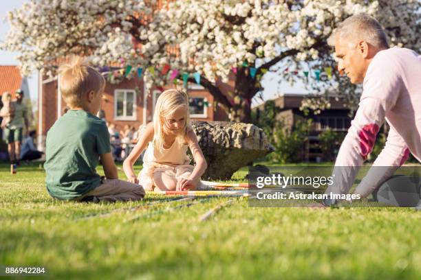 father playing giant pick up sticks with daughter (8-9) and son (4-5) in garden - mikado stock pictures, royalty-free photos & images