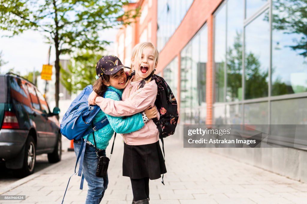 Girls (8-9) hugging and laughing by school