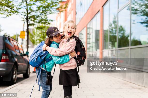 girls (8-9) hugging and laughing by school - kids backpack stock pictures, royalty-free photos & images