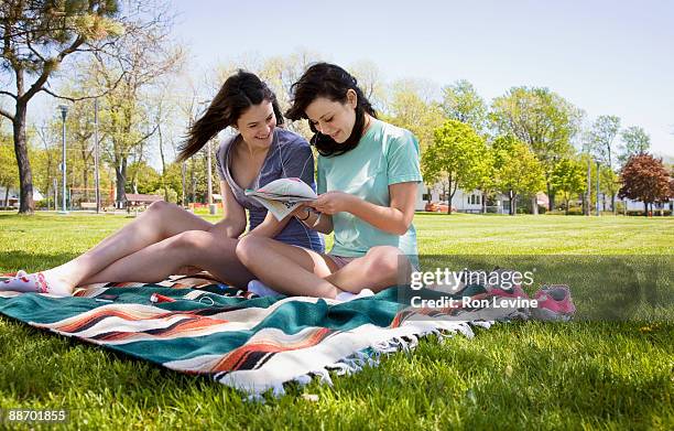teen girls looking at a magazine in a park - fille lire gazon photos et images de collection