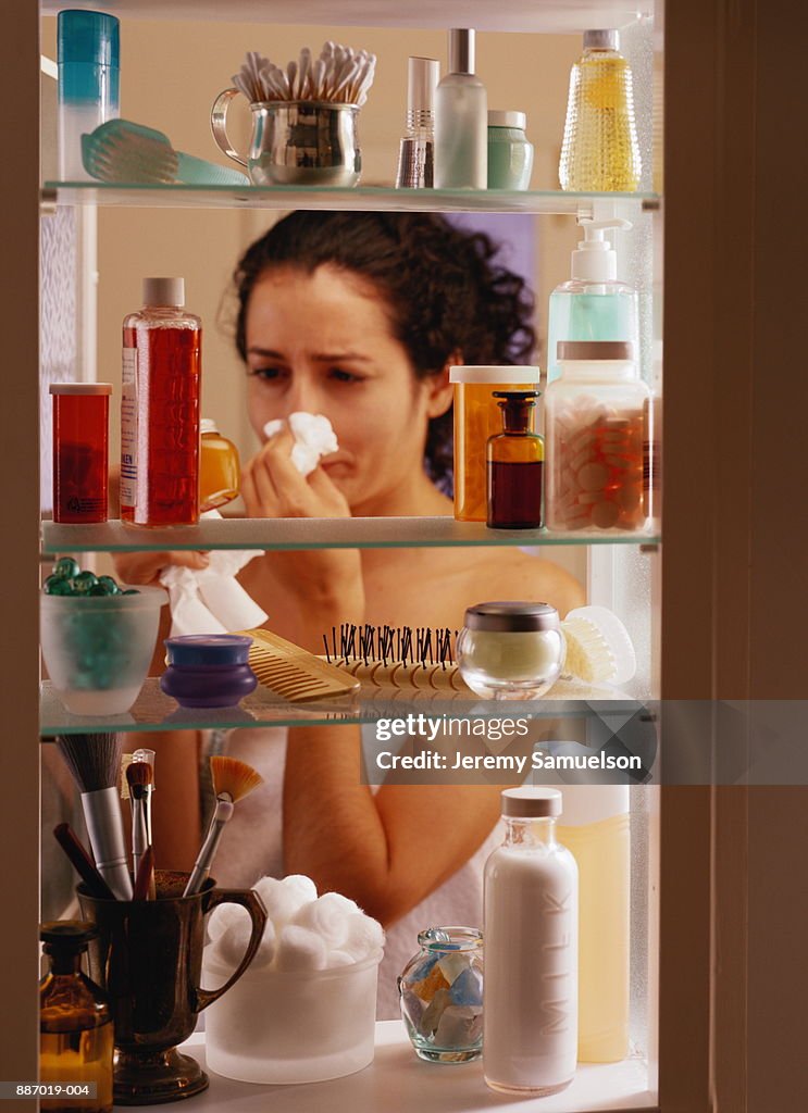 Young woman blowing nose, looking in bathroom cabinet, close-up