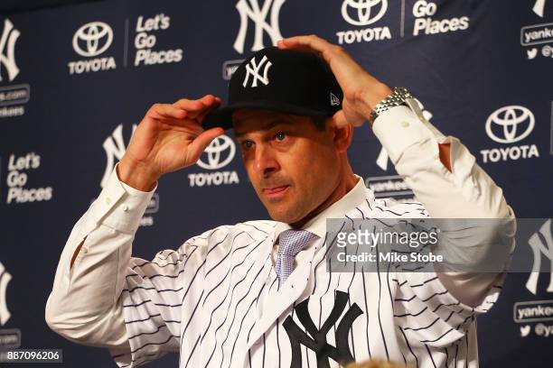 Aaron Boone puts on a Yankee cap after being introduced as manager of the New York Yankees at Yankee Stadium on December 6, 2017 in the Bronx borough...