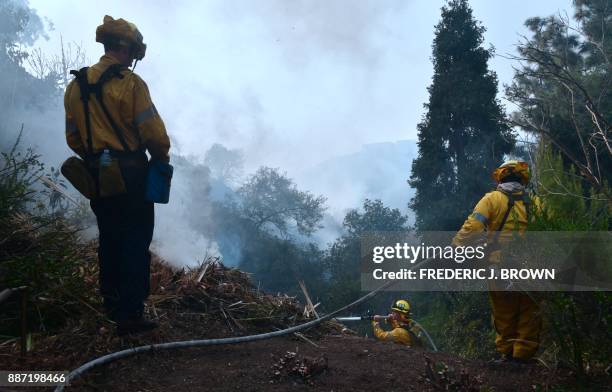 Firefighters put out sparking embers along a hillside in Bel Air, east of the 405 freeway heading north on December 6, 2017 in Los Angeles,...