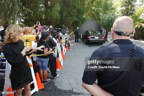 Fans, members of the media, and police watch as a family friend drives to the gate of the Jackson family mansion, where members of the family are...