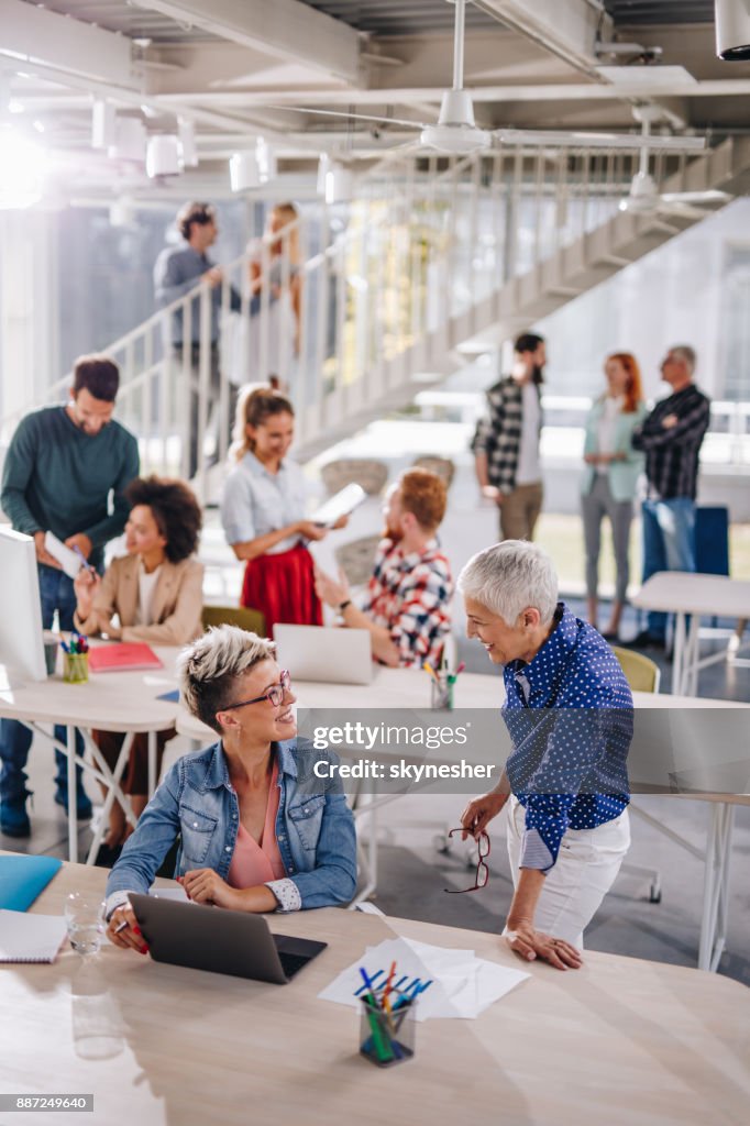 Mulheres de negócios felizes falando um com o outro no escritório corporativo cheio de pessoas.