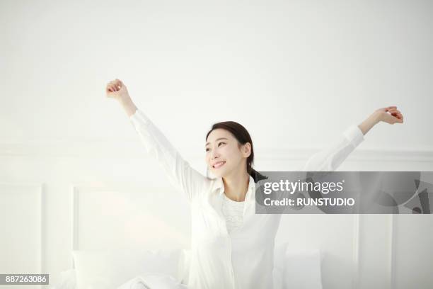 young woman smiling and stretching in bed - 腕を上げる ストックフォトと画像