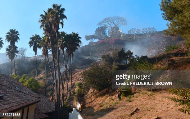 Firefighters put out burning embers on a hillside beneath homes in Bel Air on December 6, 2017 in Los Angeles, California. California motorists...
