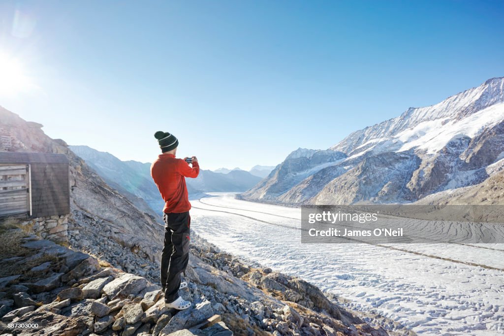 Hiker photographing glacier and mountains with phone, Aletsch Glacier, Switzerland