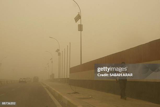 Man wearing a mouth mask walks past a wall painted in the colours of the Iraqi flag along a bridge across the Tigris River which runs through central...