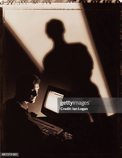 man using computer, shadow of man projected on wall (toned b&w) - suspicion office stock pictures, royalty-free photos & images