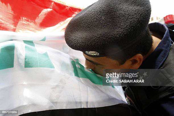 An Iraqi police officer kisses the national flag as he and a comrade decorate their police vehicle in preparation for the official withdrawal of US...