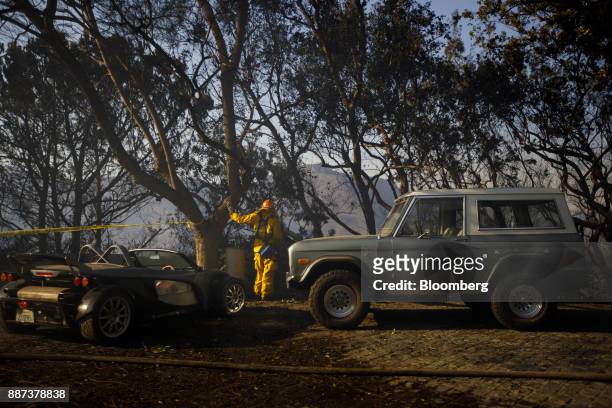Firefighter stands next to a Group Lotus Plc sports coupe and a Ford Motor Co. Bronco vehicle during the Skirball Fire in the Bel Air neighborhood of...